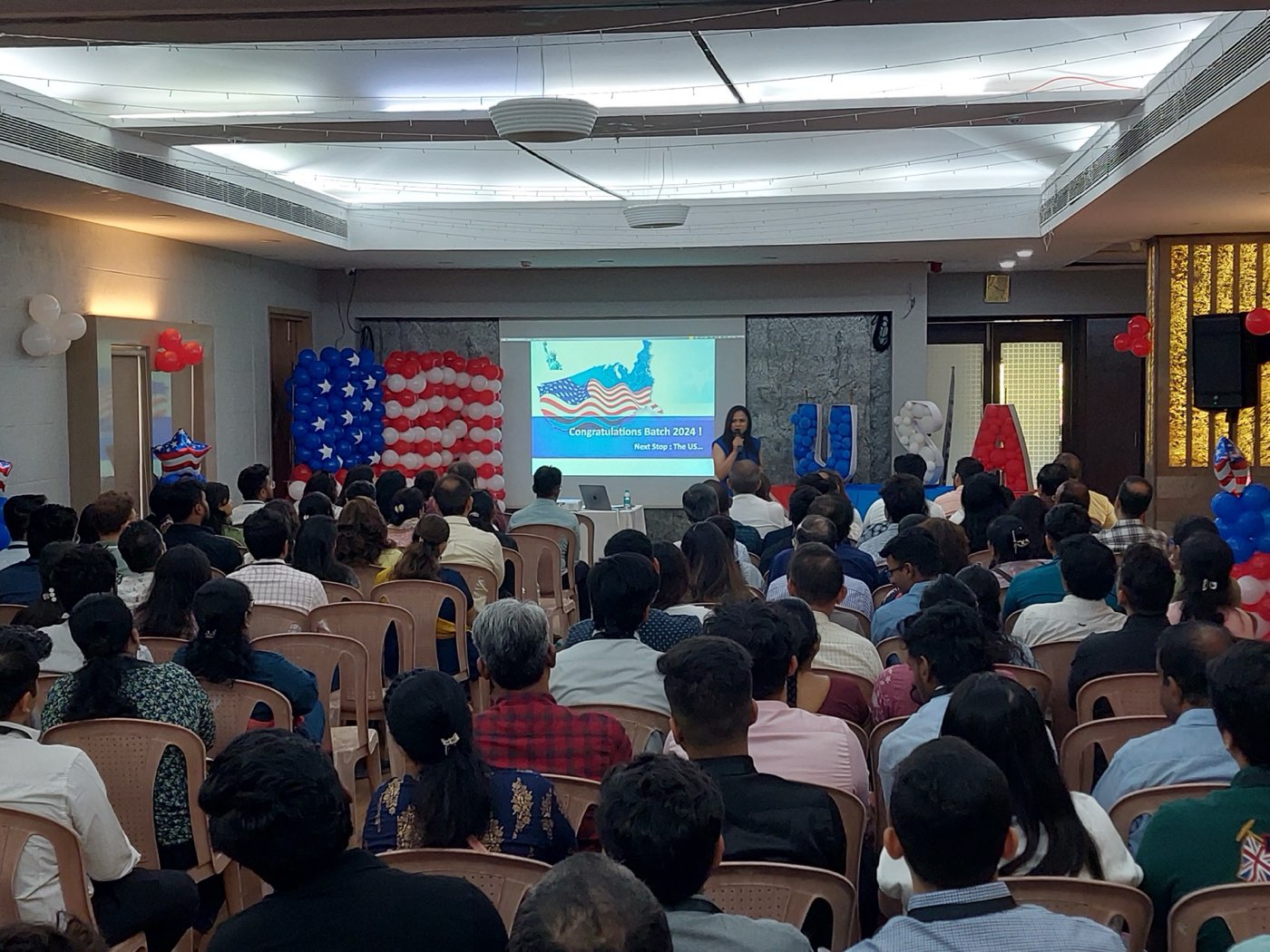 Umang Talreja addressing the goGENIUS Batch 2024 felicitation, with a hall full of students heading to the US
